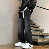 Japanese-style Drawstring Elastic-waist Jeans For Men worn with a black hoodie and white sneakers on wooden stairs.